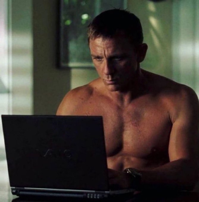 A shirtless man wearing a watch intently stares at a Sony VAIO laptop screen with a focused, slightly worried expression, capturing the universal feeling of anxiously watching crypto charts after making a trade. The dramatic lighting and his bare-chested intensity perfectly humorously convey the obsessive urge to keep checking if a sold coin is still pumping without you.