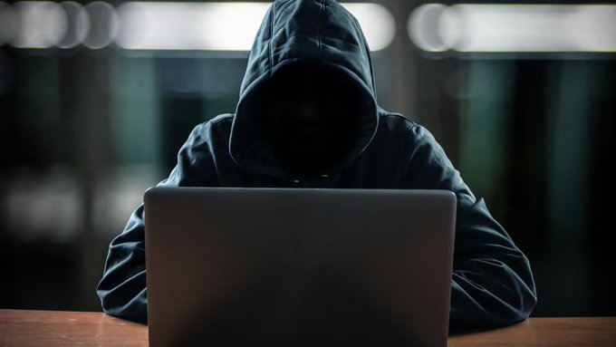 A hooded figure sits shrouded in darkness behind a laptop, evoking the shadowy, secretive nature of cybercriminals. The image visually echoes the post's reference to the Lazarus Group, a North Korean hacking organization, as Bybit takes legal action over the record-breaking $1.5 billion crypto heist.