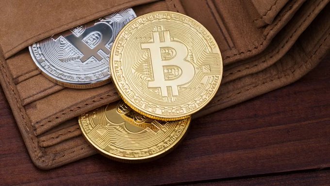 Physical Bitcoin tokens (one silver and several gold) featuring the iconic "₿" symbol and "BITCOIN DIGITAL" inscriptions rest inside a brown leather wallet, visually representing the physical storage of dormant cryptocurrency holdings that were suddenly moved after over a decade of inactivity.