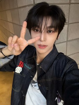 A young man with dark hair takes a selfie while making a peace sign, wearing a denim jacket with a graphic that includes the text "WOO" and Chinese characters. The casual, fan-style photo complements the post's hashtags, which appear to reference "Hershinlong," "Shinlong," and "Xinlong" (鑫隆) as an alternate name for "Alpha Drive One" (#ALD1), suggesting he is a member of the K-pop group.