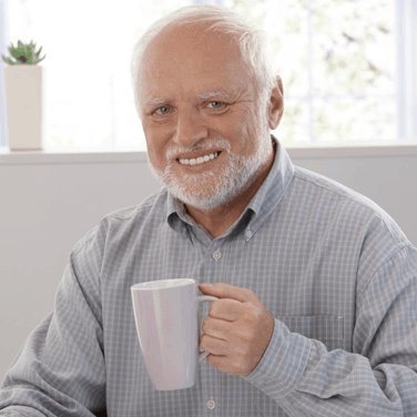 A portrait of a smiling elderly man with white hair and beard, wearing a light blue checkered shirt and holding a white mug.
