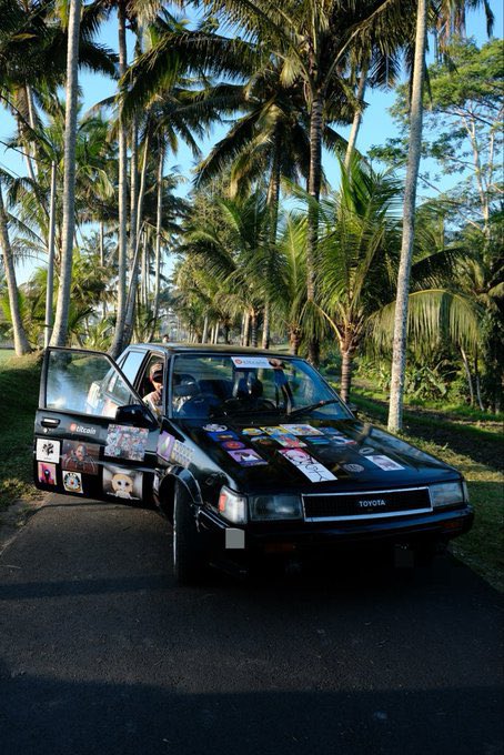 A black Toyota sedan covered in stickers parked on a road with palm trees in the background.