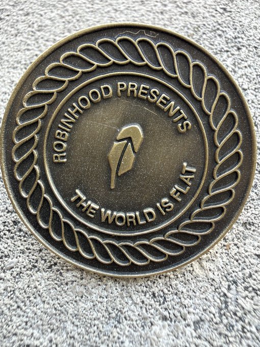 A bronze challenge coin from 'ROBINHOOD PRESENTS' featuring a flat earth symbol and the text 'THE WORLD IS FLAT' on a gray fabric background.