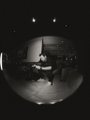The black-and-white fisheye shot captures a content creator setup with a person seated at a desk surrounded by professional lighting and camera equipment, illustrating the type of high-quality production services being offered to attendees at the Token2049 event.