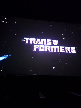 The illuminated 'TRANSFORMERS' movie logo displayed on a screen with a starry background in a dark theater.
