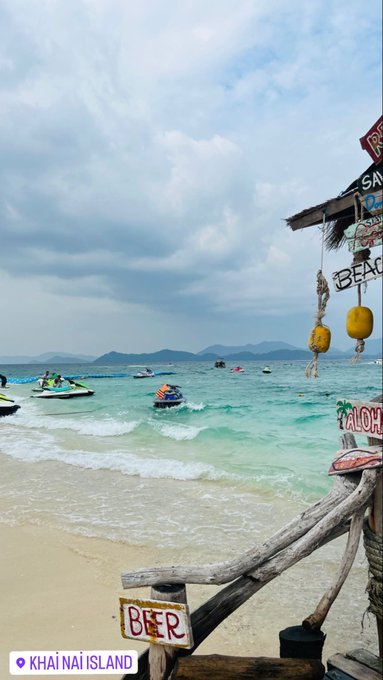Good morning from paradise ☀️—a serene view of Khai Nai Island's turquoise waters and distant jet skis, framed by rustic signs for "Beer" and "Aloha." The peaceful beach scene sets a relaxing tone to start the day.