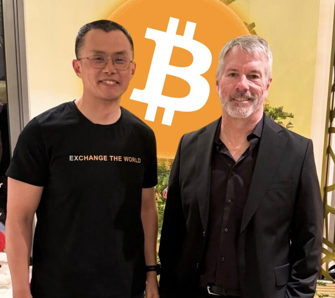 Two men pose together in front of an orange backdrop featuring a large Bitcoin "₿" logo, with the man on the left wearing a black t-shirt reading "EXCHANGE THE WORLD" — fittingly, the younger man appears to be CZ (Changpeng Zhao) of Binance, whose famous "HODL" advice aligns with the post's message about long-term crypto holding.