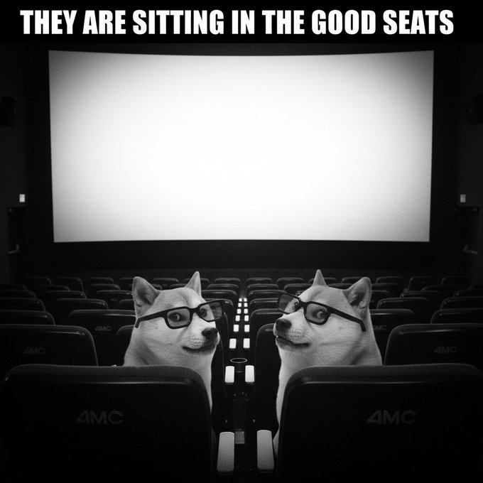 A black and white meme showing two Shiba Inu dogs wearing glasses sitting in movie theater seats with the caption 'THEY ARE SITTING IN THE GOOD SEATS'.