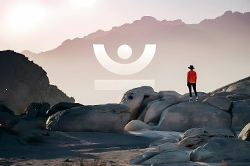 A lone figure in a red jacket stands atop rocky terrain gazing out at a vast mountain landscape, embodying the theme of community members shaping the future of JustLend DAO through governance and voting. The JustLend logo is subtly overlaid in the center of the image, reinforcing the connection between the individual's perspective and the collective decision-making process described in the accompanying post.