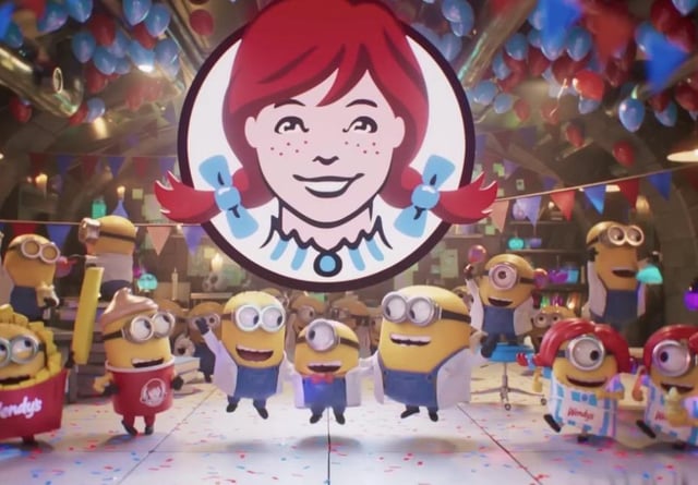 A Wendy's logo is displayed above a group of Minions in a festive, party-themed setting with balloons and confetti. The "$WEN" ticker relates to the image as it references Wendy's, the fast-food brand featured prominently in the scene.