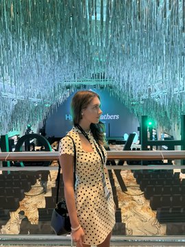 A woman wearing a polka-dot dress and glasses stands in front of a striking indoor installation of hanging blue fiber-optic lights.