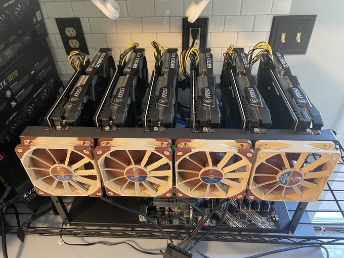 A cryptocurrency mining rig setup featuring multiple MSI GeForce RTX graphics cards (appears to be RTX 3070 models) with brown/tan colored fans mounted on a metal frame against a tiled wall.