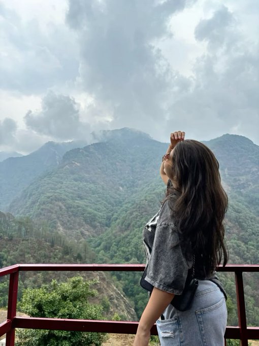 The image features a woman standing on a balcony, looking out at a beautiful mountain range with her hair blowing in the wind. She appears to be enjoying the view or contemplating something. The photo has been captioned "eraly Morning Web3 good Morning @base Family good morning @Polymarket Fam Creator Active 2K RT". This suggests that the image was taken during an early morning, possibly on a weekend or holiday when people have more free time for outdoor activities and sightseeing.