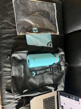 The image features a black leather couch with various items placed on top of it, including a backpack, a water bottle, and a laptop computer. The backpack appears to be a messenger bag or a backpack-style handbag, while the water bottle is a blue sports bottle. A laptop computer can also be seen in the scene, suggesting that someone might have been working or studying from home. The image seems to be related to a post about using a wallet for Bitcoin transactions, as indicated by the use of terms like "BG Wallet" and "Bitget Wallet CN".