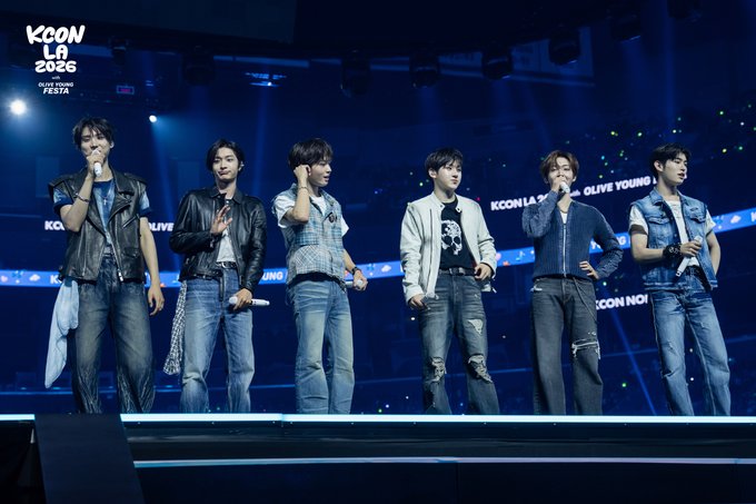 Six members of K-pop group KickFlip perform on stage at KCON LA 2026, as indicated by the "KCON LA 2026" logo and "OLIVE YOUNG FESTA" text visible in the image, matching the M COUNTDOWN Stage recap from Day 1 of the August 14-16 event at Crypto.com Arena.