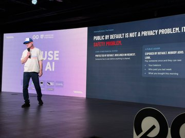 A presenter stands on a stage delivering a presentation with the visible slide title 'PUBLIC BY DEFAULT IS NOT A PRIVACY PROBLEM...' and 'ABUSE AI BEING A SAFETY PROBLEM'.