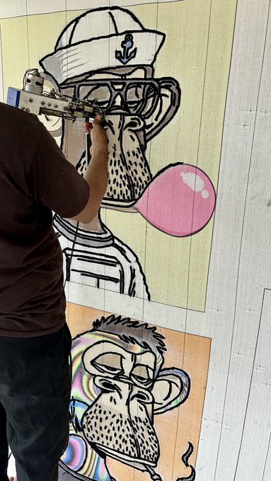 An artist working on a large mural depicting a cartoon monkey wearing a captain's hat and glasses while blowing a pink bubblegum bubble.