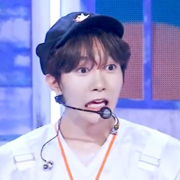 A young man on what appears to be a television set wears a dark cap and a headset microphone, looking surprised with wide eyes and an open mouth.