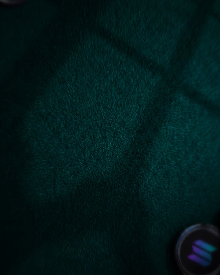 The image shows a close-up view of a green surface with a shadow cast by a light source, possibly a lamp or a light fixture. The background appears to be a dark color, which contrasts with the green surface and makes it stand out. There are two small circles in the bottom right corner of the image, but they do not seem to have any significance other than being part of the overall composition.