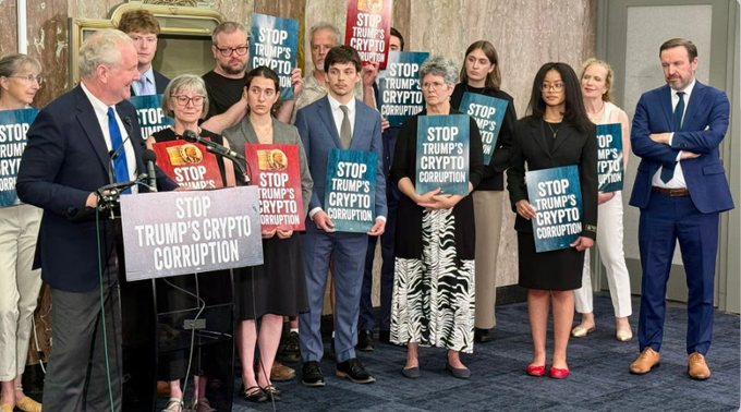Press conference with a group of officials holding blue 'STOP TRUMP'S CRYPTO CORRUPTION' signs at a podium during a political event.