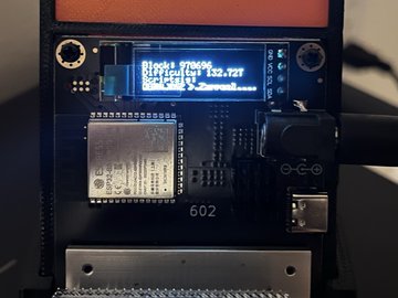 A close-up of an ESP32 microcontroller board (labeled "602") with an attached OLED screen displaying "Risk to fee" data and "2.127", connected to a USB-C cable and an SD card adapter.