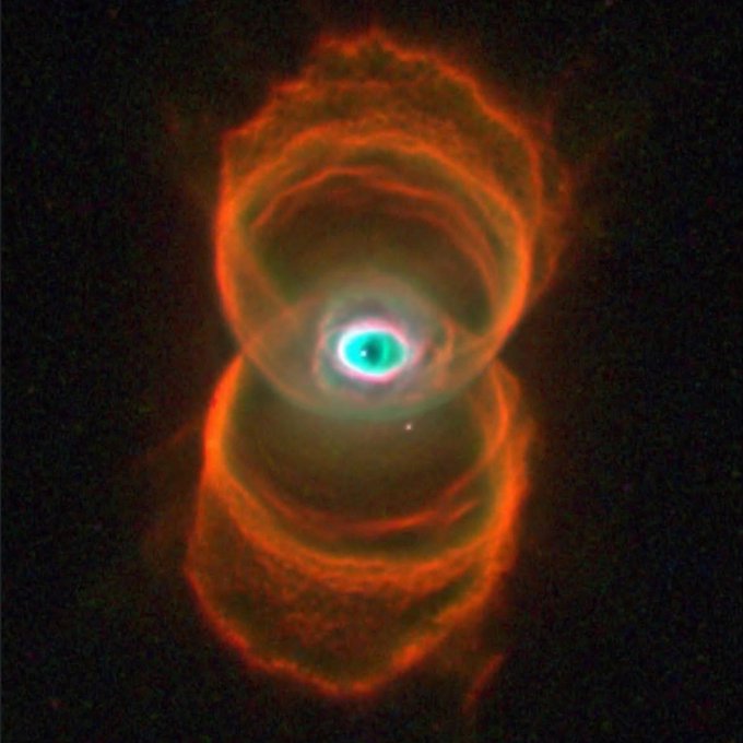 An astrophotography image of the Stingray Nebula, showing a bright central star with glowing concentric rings of orange-red gas surrounding it against a dark background.