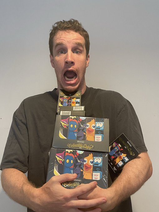 A man with an excited, open-mouthed expression holds a large stack of "Collectible Cards" featuring cartoon bird characters, including one labeled "NEW DROP."