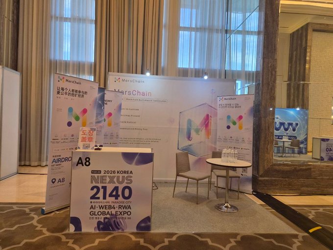 MarsChain booth setup at the 2026 NEXUS 2140 AI·WEB4·RWA Global Expo (Hall A8), featuring promotional banners, branded displays, and a small meeting area with table and chairs in the venue. The image showcases the sponsor's exhibit space where visitors could experience MarsChain's blockchain solutions firsthand.
