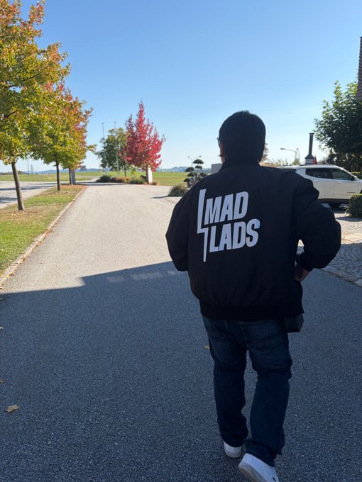 A person walks down a paved pathway wearing a black bomber jacket with "MAD LADS" printed in bold white letters on the back.
