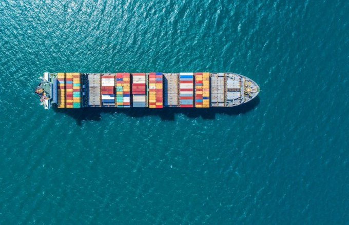 An aerial view of a cargo ship loaded with colorful shipping containers sailing on blue water.