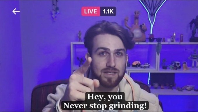 Screenshot of a live stream by a bearded young man in a hoodie, showing 1.1K viewers with the subtitle 'Hey, you Never stop grinding!' displayed at the bottom.