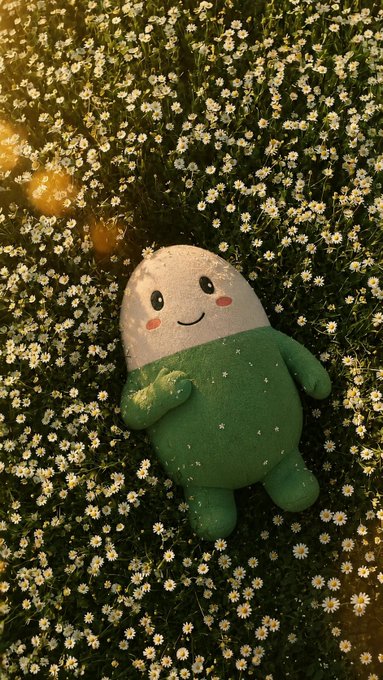 The image shows a plush green and white mascot doll with a smiling face lying in a field of small white daisies, bathed in warm sunlight. The mascot resembles "$Cupsey," the official mascot of the popular meme token Cupsey on Solana, complementing the post's playful reference to "the cutest sleeper" in crypto.