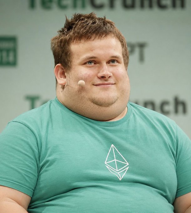 A man with short brown hair wearing a headset microphone and a teal t-shirt with the Ethereum logo smiles during a panel, likely at a TechCrunch Disrupt event.