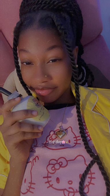 The image features a young woman with long braids wearing a Hello Kitty shirt, holding a drink or snack while sitting down. The scene appears to be set in a room where there are chairs around her. There's also an element of technology present, as she is using a cell phone. The image does not provide any information about the content on the post or its relation to the woman and her surroundings.