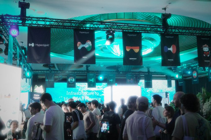 A crowded technology exhibition booth labeled “Hyperliquid” hangs banners for “SUSHI,” “GERMANY,” and “FRANCE,” with a large screen reading “Infrastructure to Hyper...Alliances.”