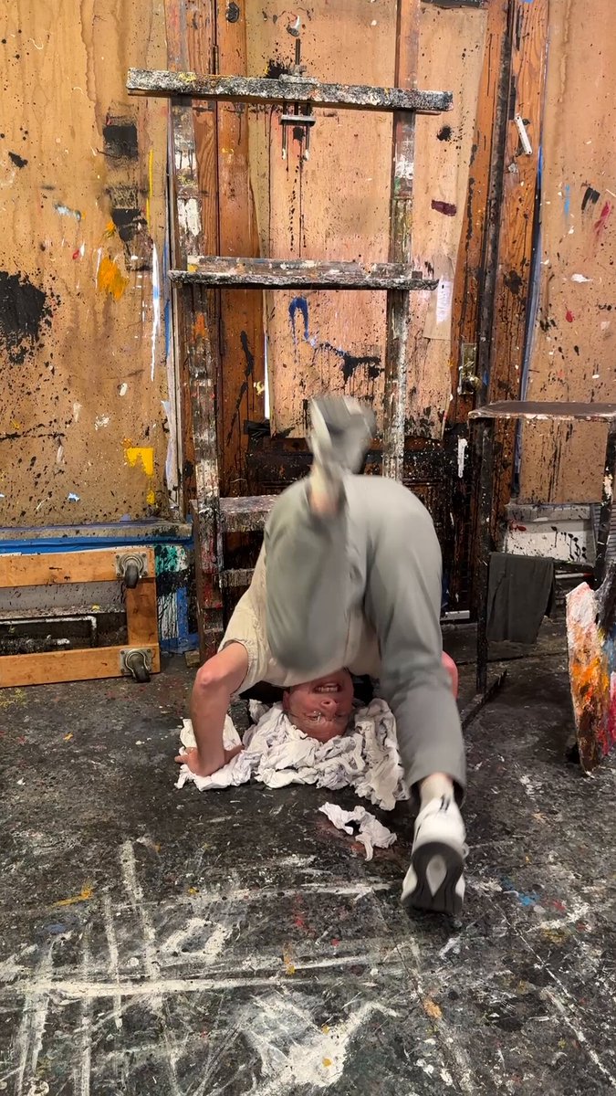 The image features an artist performing a handstand against a wall with paint splatters. The artist's legs are hanging off the ground as they balance upside down, creating a sense of instability or vulnerability. The painting "Petals" by the artist is displayed in the background, and it appears to be about fragility, intimacy, and memory. The image also includes text that reads: "Petals— Ordinal drop Next Tuesday June 9, 18 edition 0.0025 BTC A new work bridges BTC and ETH An Ordinal on BTC Every collector gets a music track on Eth Links to both 'Petals' is about fragility, intimacy, and the way memory lingers after a moment has passed."