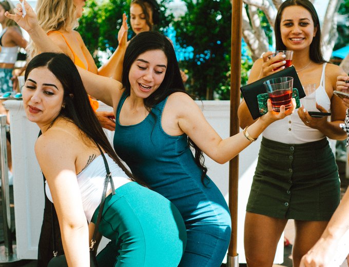 Three young women enjoying drinks and dancing at an outdoor party in sunny weather.