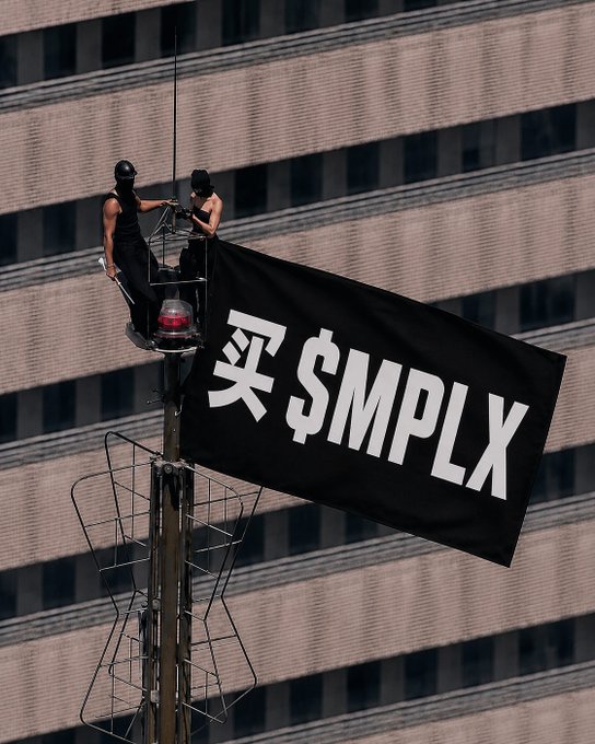 Two climbers in black balaclavas perch atop a tall structure against a skyscraper backdrop, unfurling a black flag reading '买 $MPLX'.