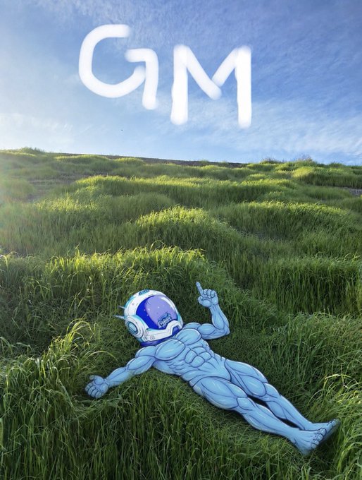 A muscular blue alien character with a helmet lies in a grassy field pointing upward, with the word "GM" written in sky-writing in the clouds above.