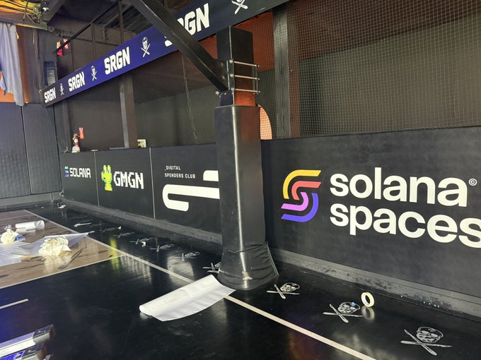 An indoor sports or gaming venue features a black basketball hoop pillar with branding for 'SRGN', 'GMGN', 'Solana Spaces', and 'Digital Spenders Club' on the walls.