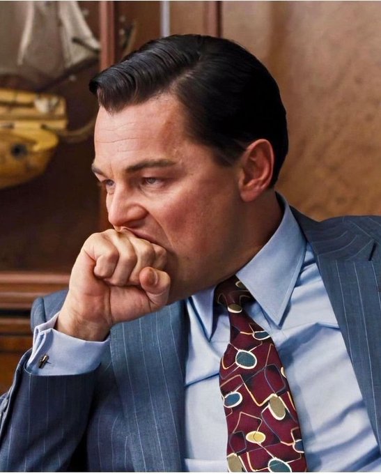 A portrait of Leonardo DiCaprio as a man in a pinstripe suit and patterned tie, with his hand near his mouth in a thoughtful pose.