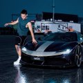 A young man in a gray t-shirt and dark pants poses on the hood of a silver sports car at night.