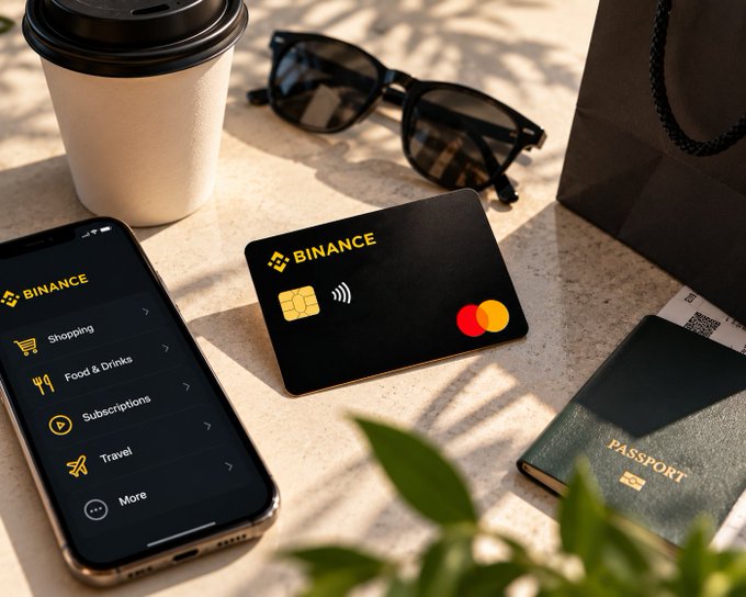 A Binance Card rests on a sunlit surface alongside a coffee cup, sunglasses, a passport, and a smartphone displaying the Binance app's spending categories (Shopping, Food & Drinks, Subscriptions, Travel), illustrating how the card integrates crypto into everyday purchases. The image visually reinforces the post's theme of making crypto practically spendable in real-world scenarios like travel and dining.