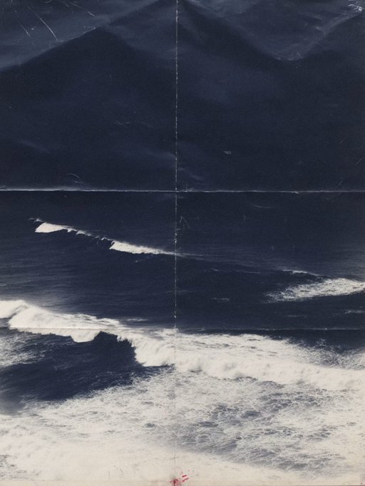 An aerial view of ocean waves crashing toward a sandy beach with dark mountains or cliffs in the background, rendered in a vintage film-like aesthetic with visible vertical lines.