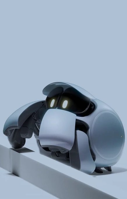 A small, rounded silver robot with glowing oval eyes and articulated limbs perched on a white ledge against a light blue background.