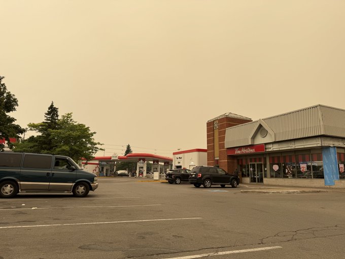 A hazy, smoke-filled street scene shows a gas station, a Tim Hortons restaurant, and several parked vehicles under an orange-tinted sky.