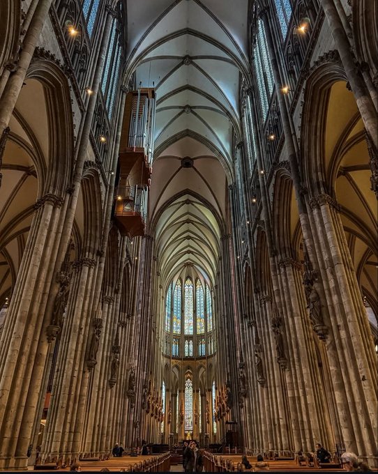 The interior of a Gothic cathedral features soaring vaulted ceilings, tall columns, and stained glass windows.