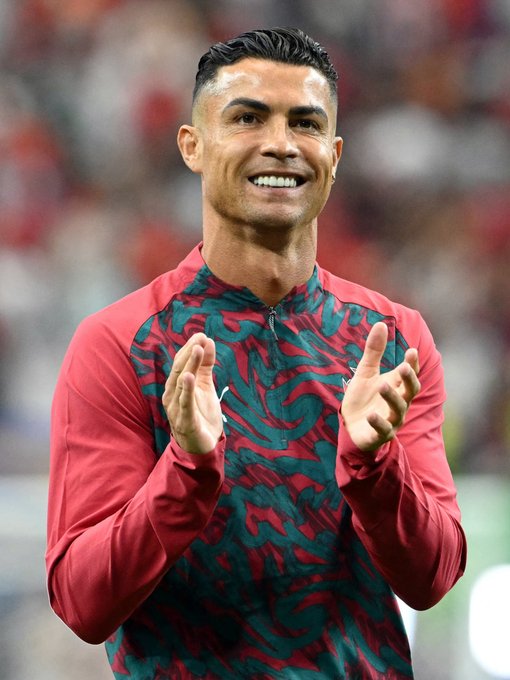 Photograph of soccer player Cristiano Ronaldo smiling and clapping while wearing a red and teal training top.