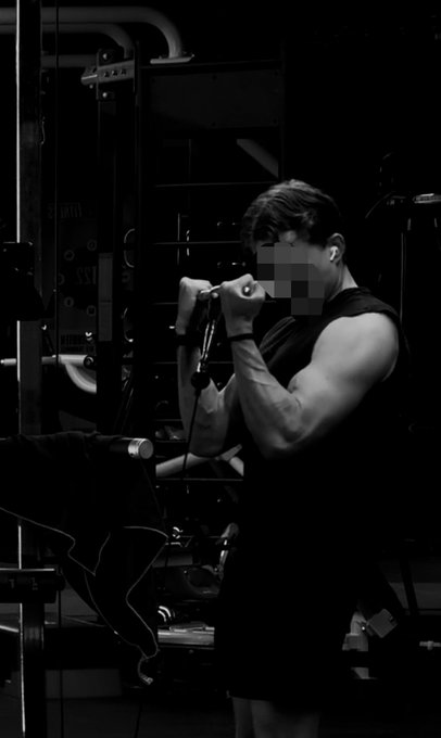 Black and white photo of a person performing a cable exercise at the gym, wearing a sleeveless shirt, with their face pixelated.
