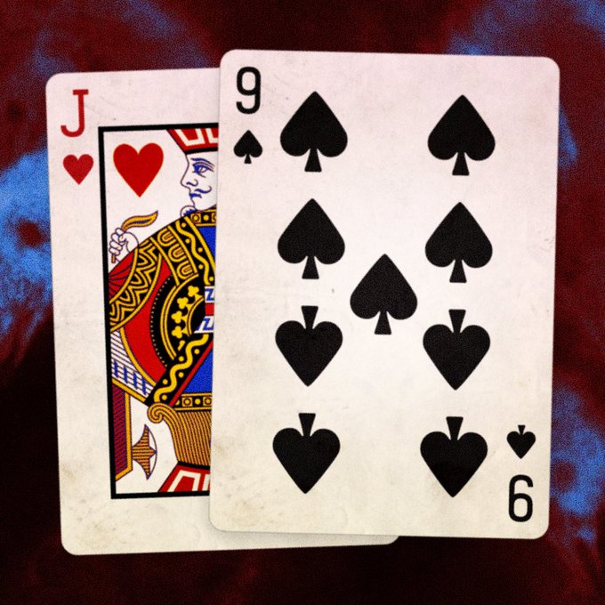 Two playing cards, the Jack of Hearts and the 9 of Spades, lie overlapping on a dark red and blue patterned fabric background.